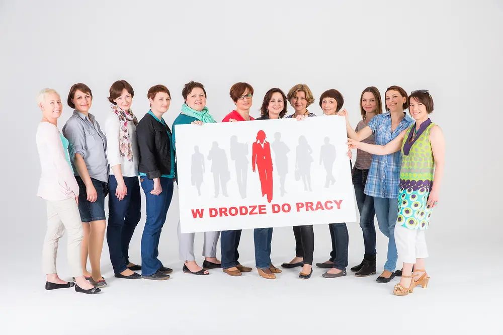 Women standing together with the “W drodze do pracy” sign