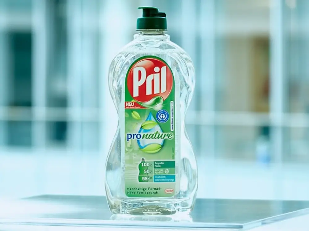 A bottle of the dishwashing product Pril Pro Nature standing on a transparent table.