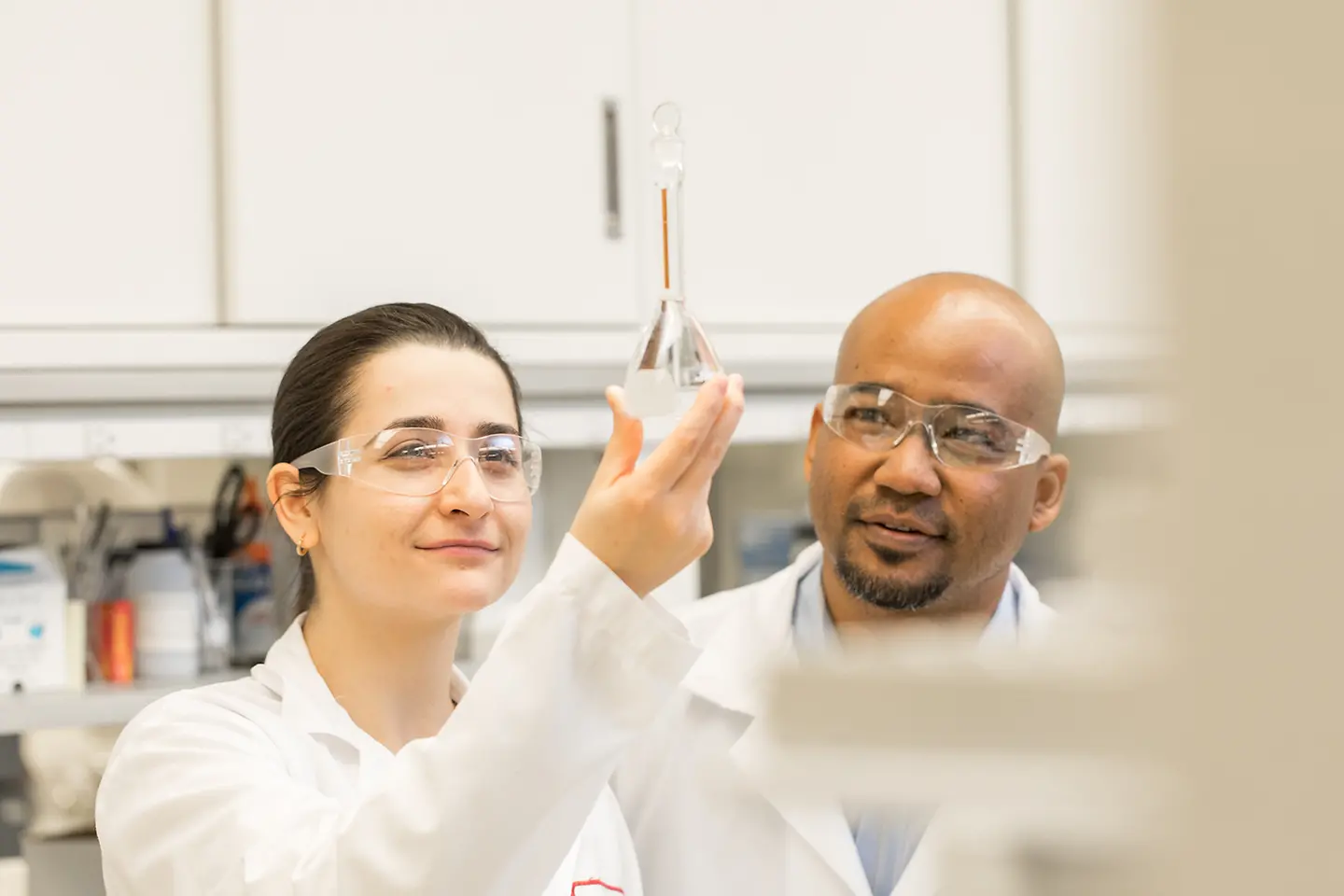 A female and a male lab worker contemplate a liquid in a vial